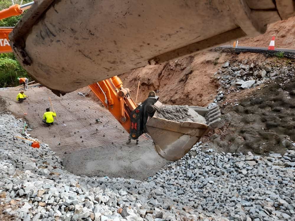 A Large Excavator Is Digging A Hole In The Ground Filled With Rocks — Ingham Concrete–Icon in Ingham, QLD