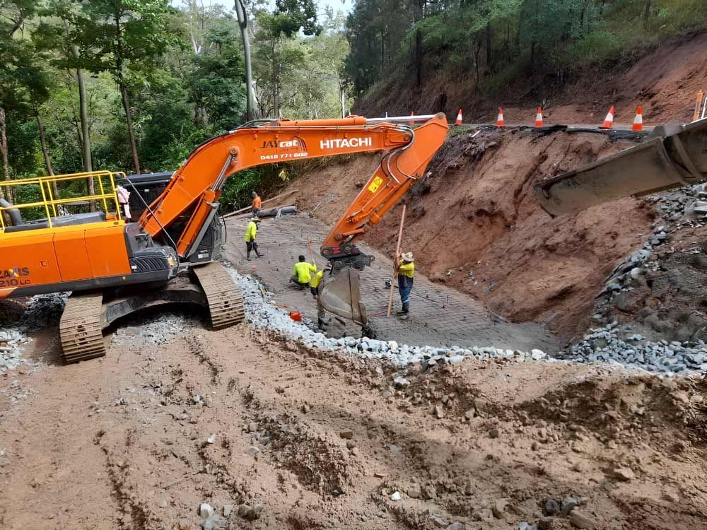 A Large Orange Hitachi Excavator Is Working On A Dirt Road — Ingham Concrete–Icon in Ingham, QLD