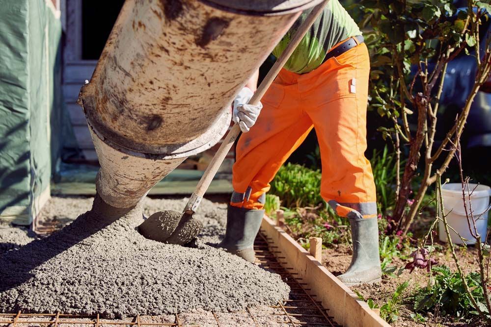 A Man Is Pouring Concrete Into A Hole With A Shovel — Ingham Concrete–Icon in Cardwell, QLD