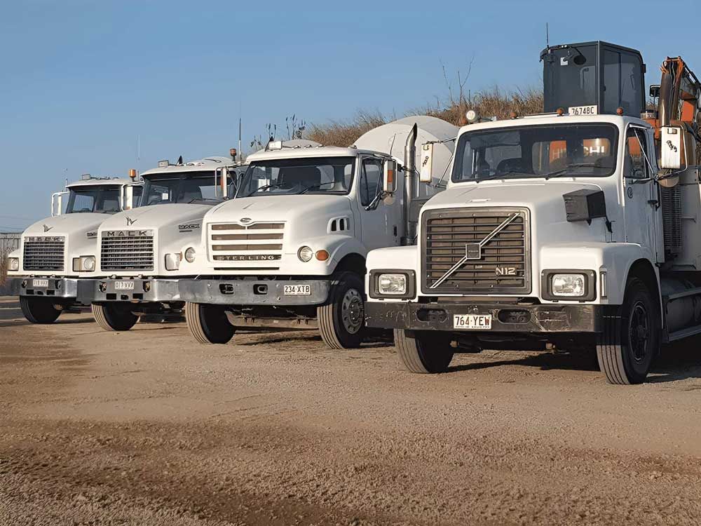A Row Of Volvo Mixer Trucks Are Parked In A Gravel Lot — Ingham Concrete–Icon in Ingham, QLD