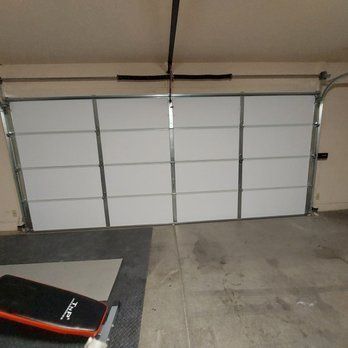 A white garage door is open in a garage next to a bench.