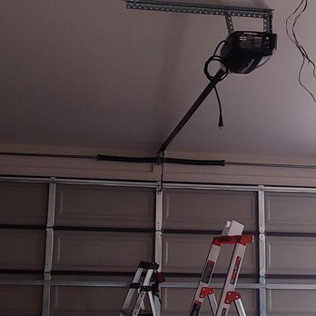 A garage door opener is hanging from the ceiling next to a ladder.