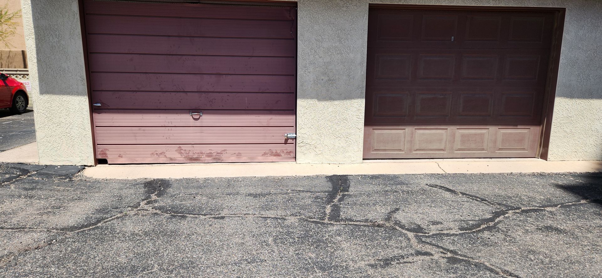 A red car is parked in front of two garage doors.