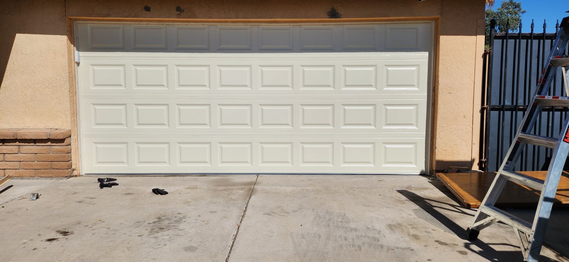 A white garage door is being installed in a driveway next to a ladder.