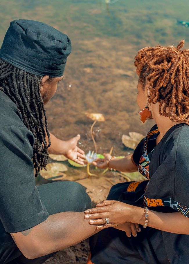A man and a woman are sitting next to each other in front of a pond holding hands.