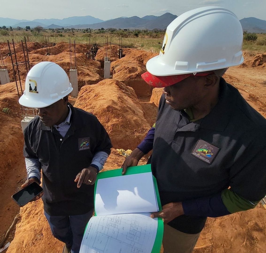 Two men wearing hard hats are standing in a dirt field