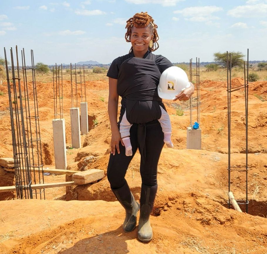 A woman is holding a baby and a hard hat