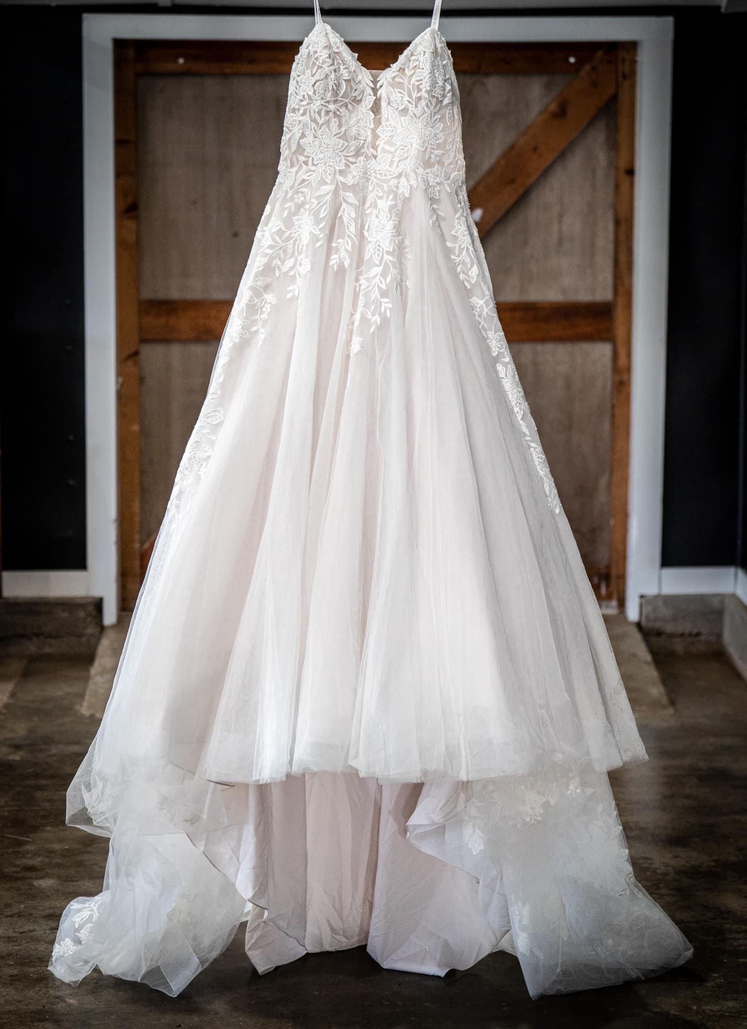 White wedding dress hanging in front of a wooden door.