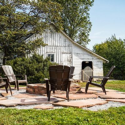Adirondack chairs around a fire pit on a stone patio, with a white barn in the background.