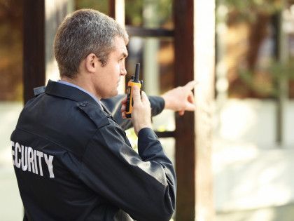 Security guard in uniform points while holding a radio, outdoor setting.