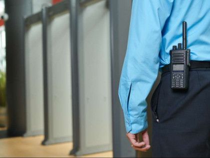 Security guard in a light blue shirt and dark pants with a walkie-talkie at their hip.
