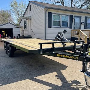 A flatbed utility trailer with new wooden planks parked in front of a white residential house.