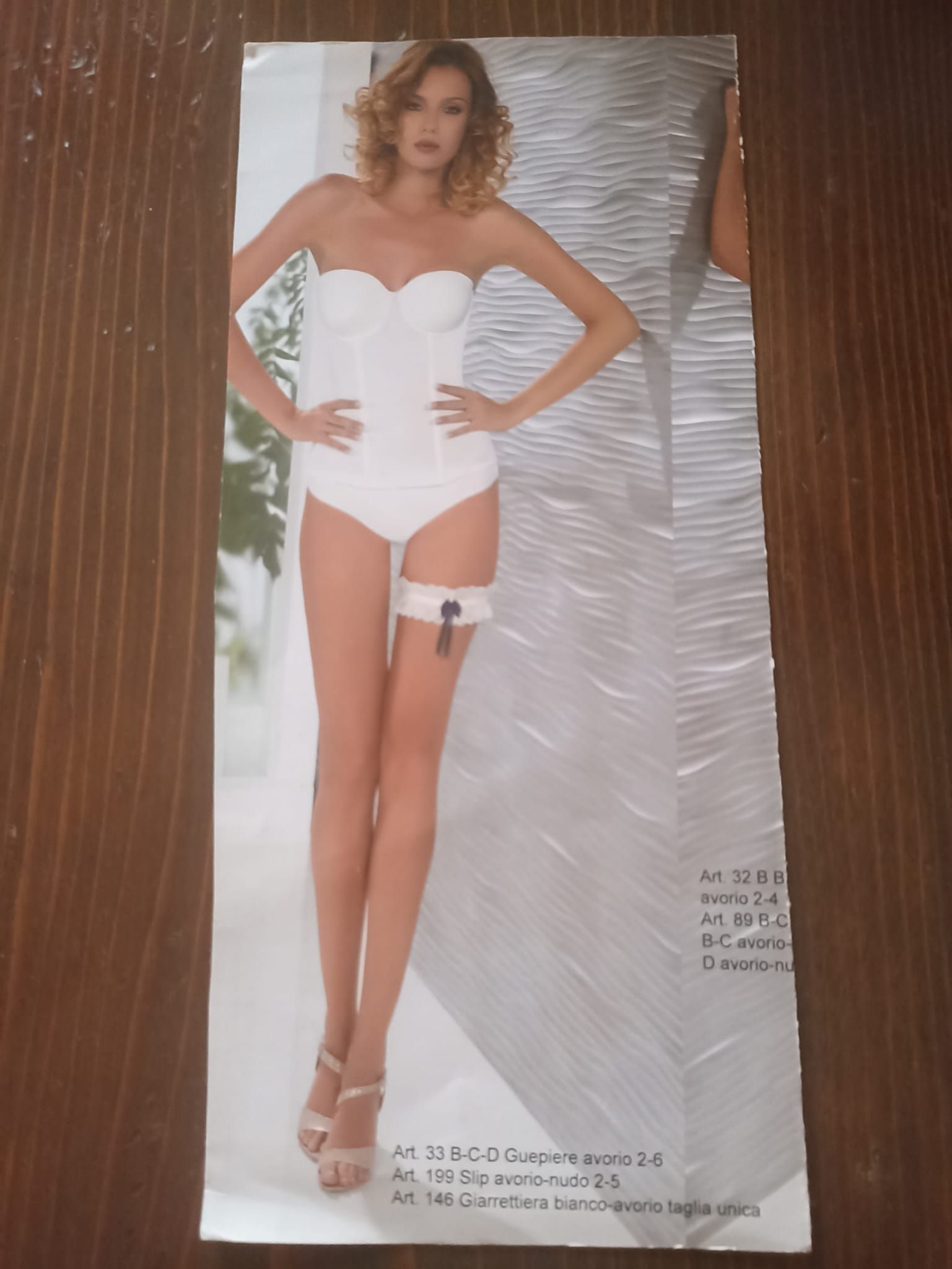 Donna in lingerie bianca, in piedi con le mani sui fianchi, con giarrettiera. Sfondo bianco.