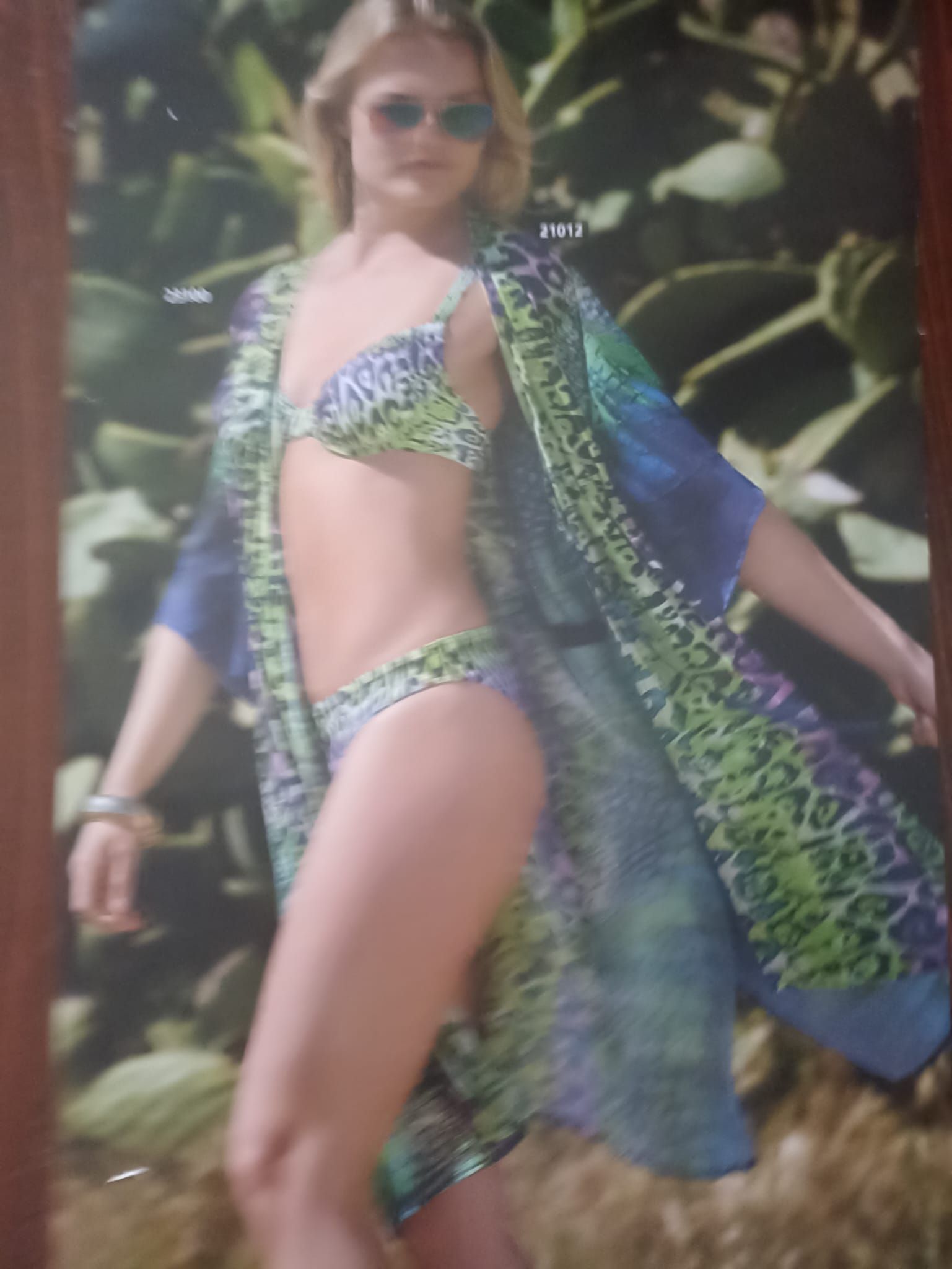 Donna in bikini e vestaglia, in piedi all'aperto. La vestaglia e il bikini hanno una fantasia blu e verde.