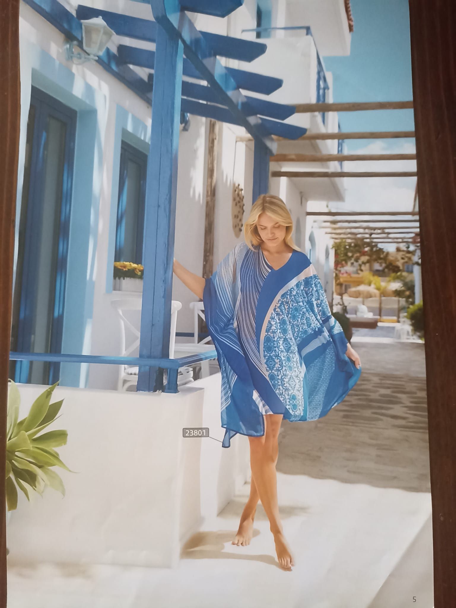 Donna con copricostume blu fantasia su un balcone bianco con dettagli blu.