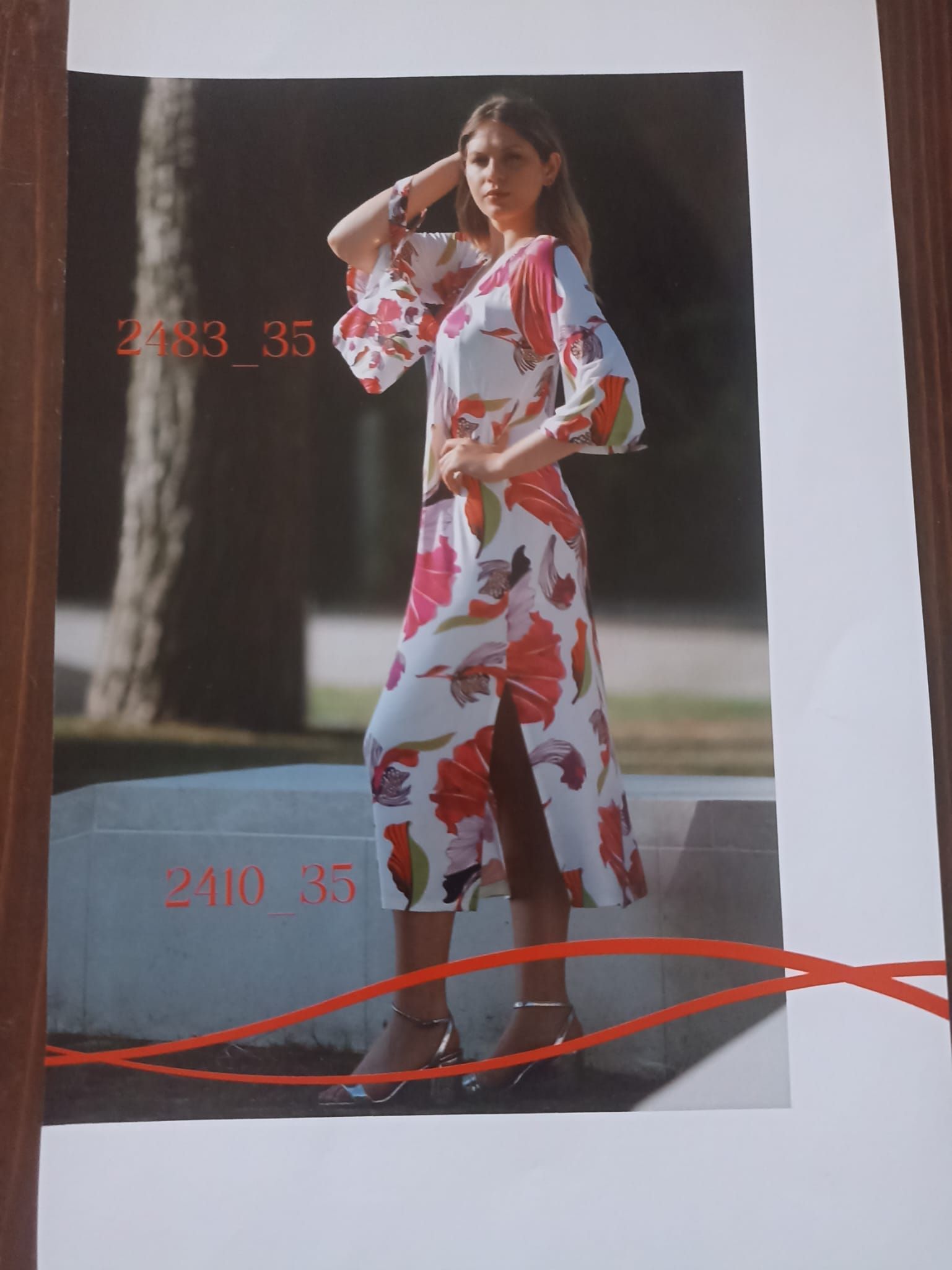 Donna in abito bianco a fiori con spacco laterale in posa all'aperto.