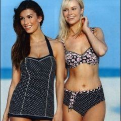 Due donne in costume da bagno sorridono su una spiaggia. Una con un top a pois e pantaloncini coordinati, l'altra con un bikini a fiori.