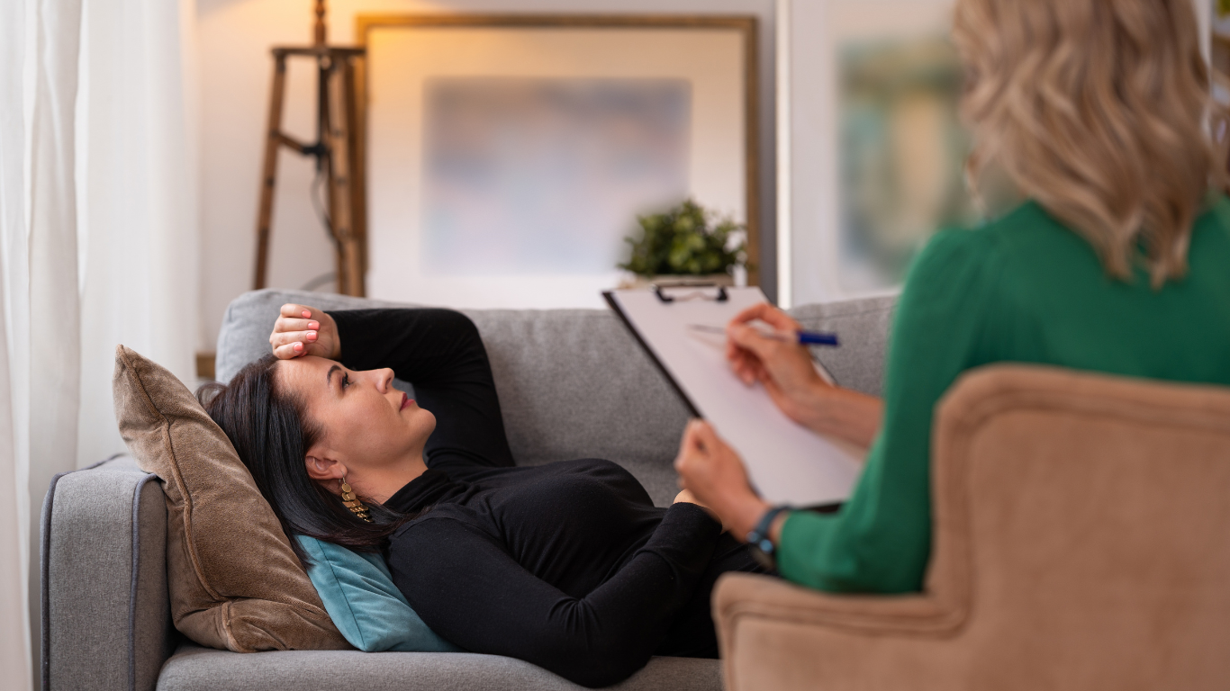 A woman is laying on a couch talking to a therapist.