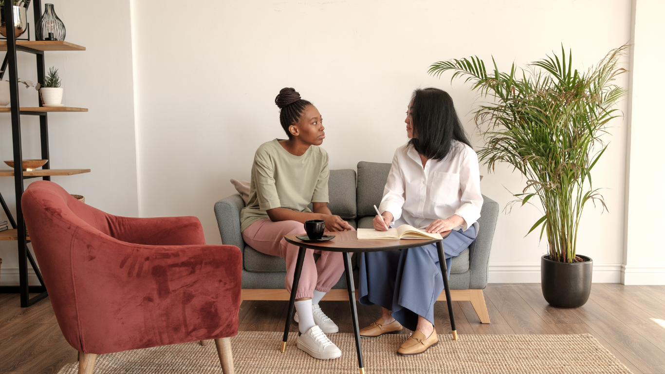 Two women are sitting on a couch talking to each other.