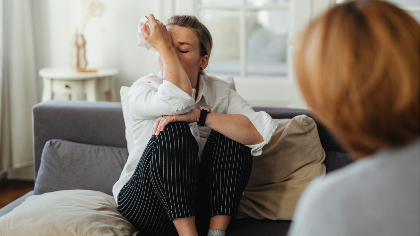 Woman in a counseling session, gesturing with a tablet while speaking to another woman in a modern office.