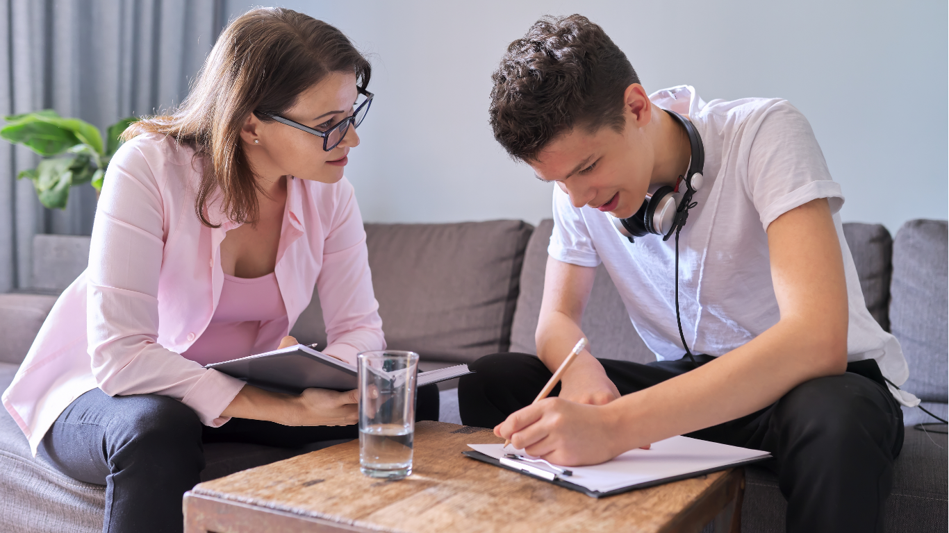 Group therapy session: Five diverse people sit in chairs, one therapist gesturing, all engaged in discussion.