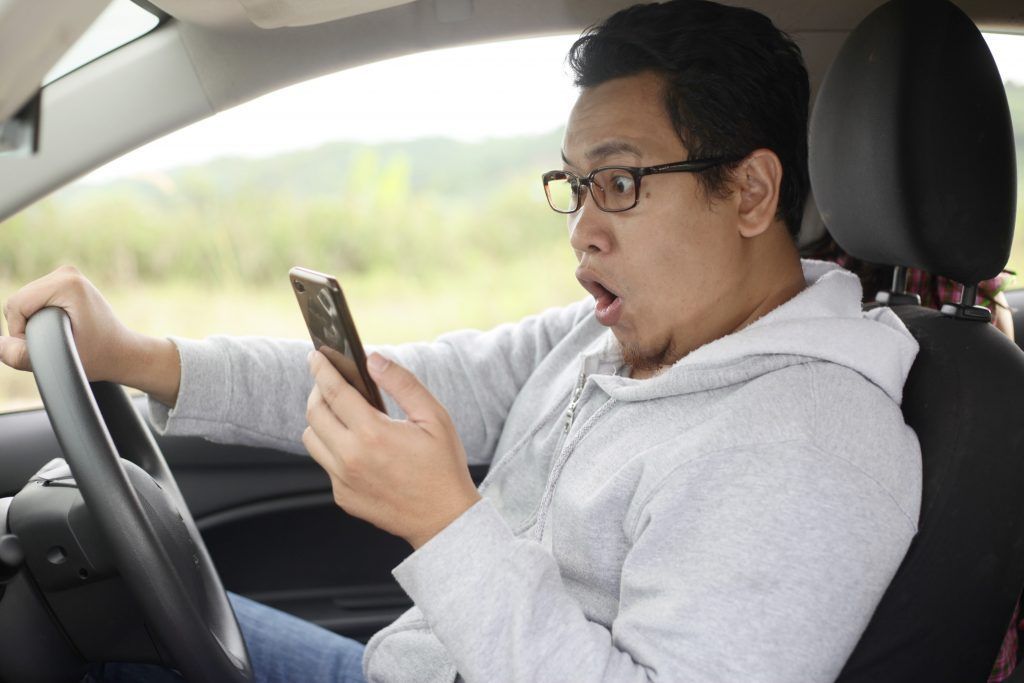 A man is sitting in a car looking at his cell phone.