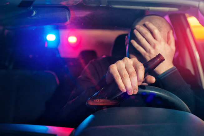 A man is sitting in a car holding a bottle of alcohol.