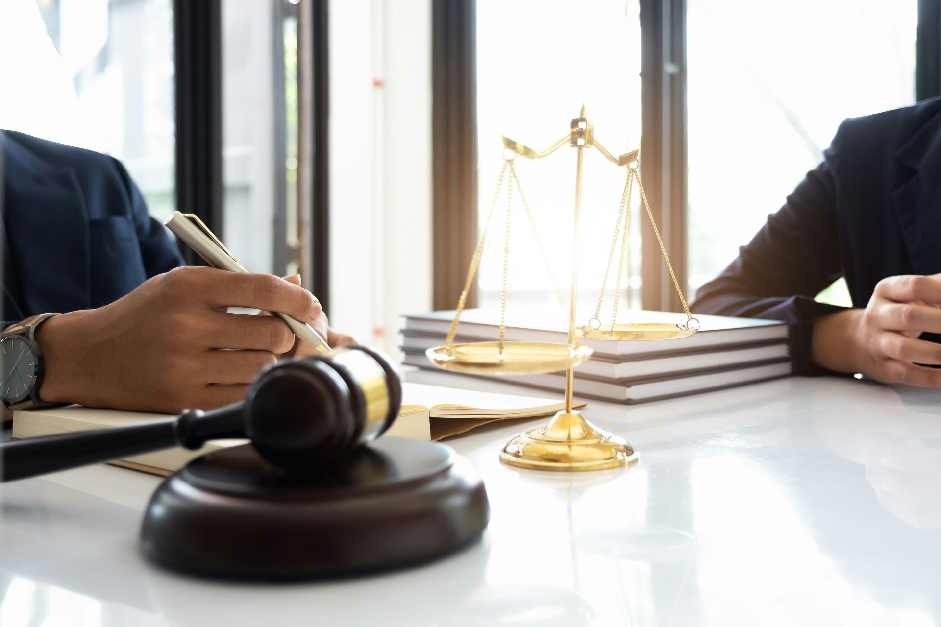 A couple of people are sitting at a table with a gavel and scales of justice.