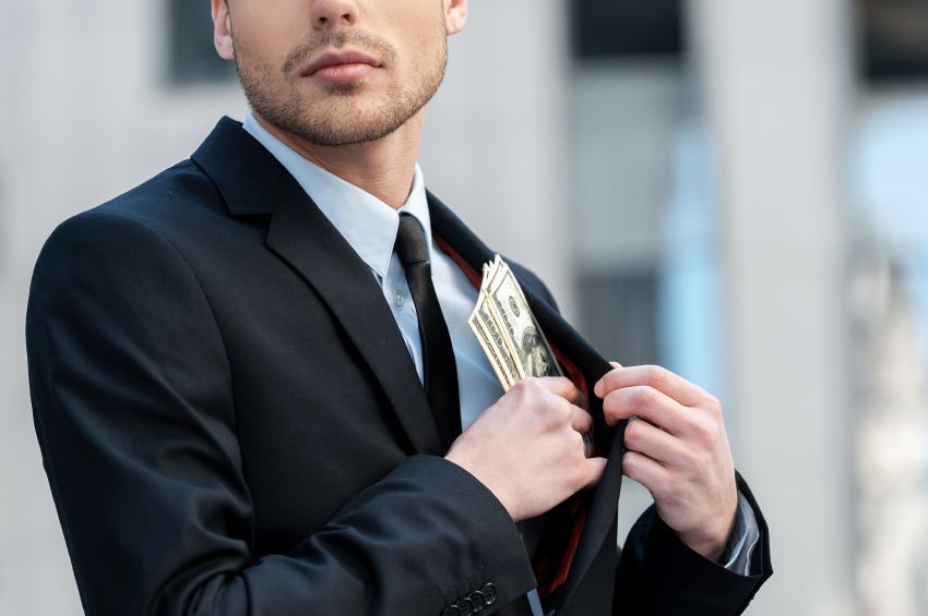 A man in a suit and tie is putting money in his pocket.