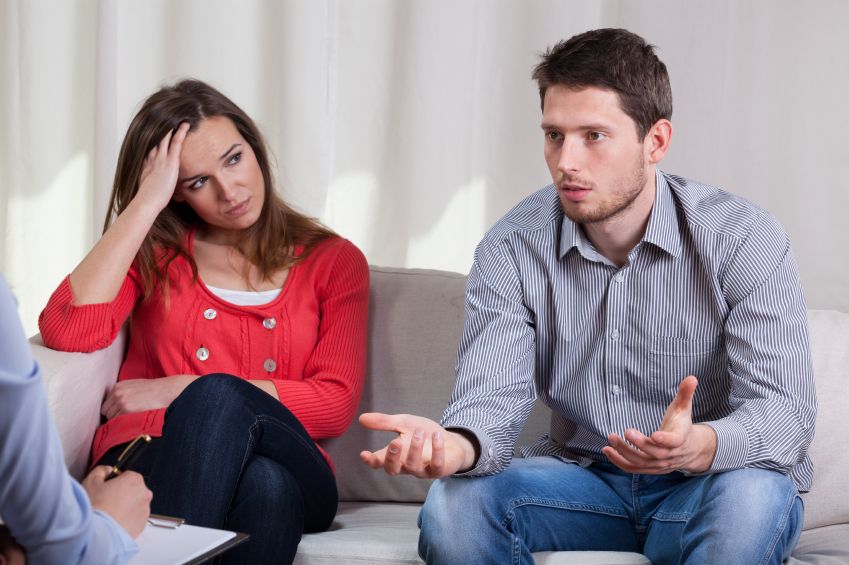 A man and a woman are sitting on a couch talking to a counselor.