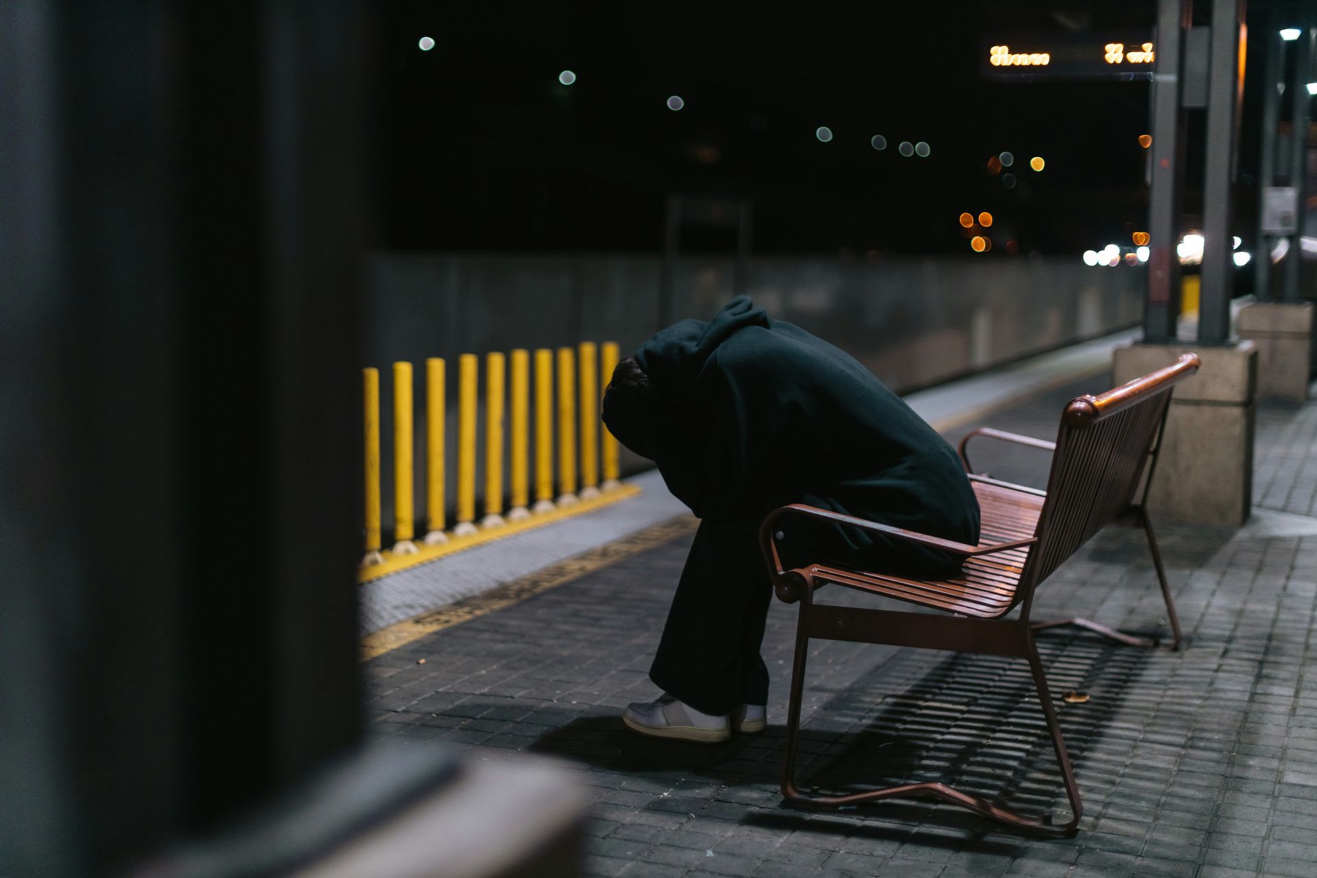 A person is sitting on a bench with their head down at night.