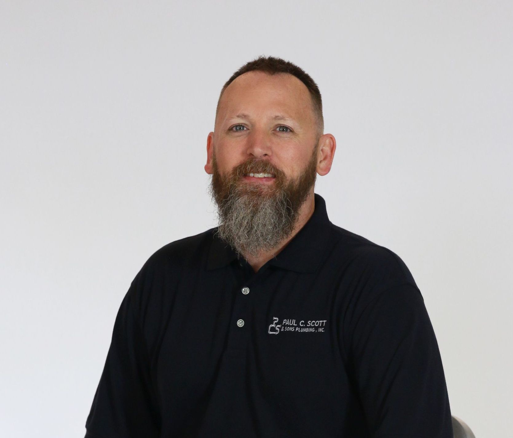 A man with a beard is wearing a black polo shirt.