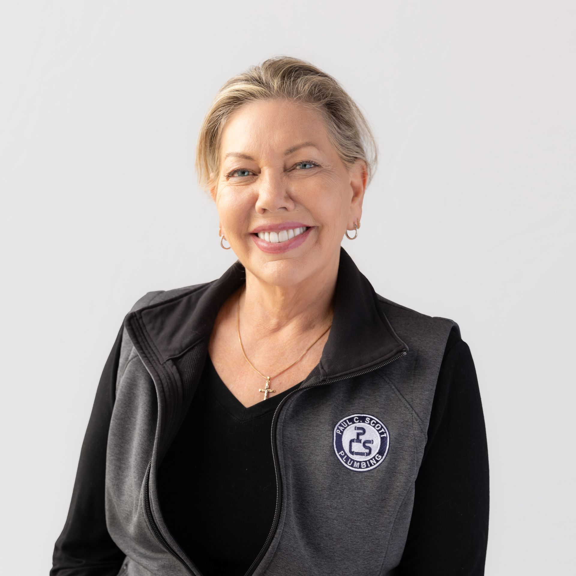A woman wearing a black sweater and a white shirt is smiling for the camera.