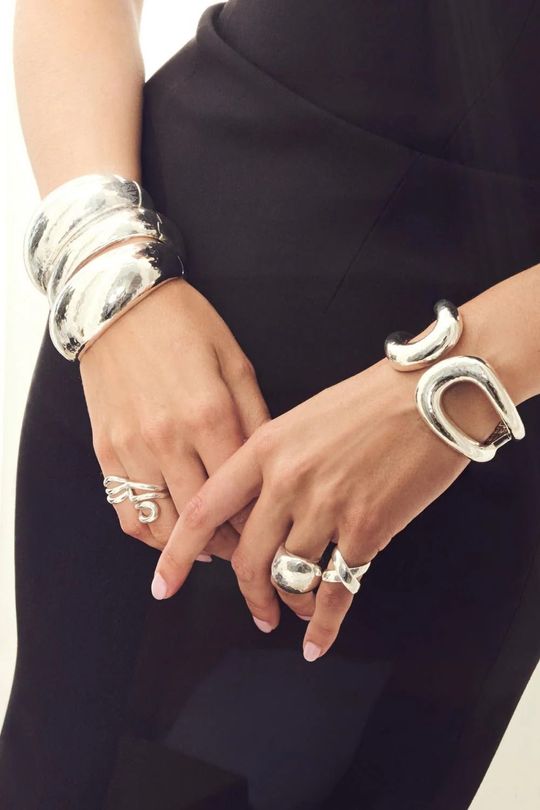 Woman wearing silver bracelets and rings on a black dress.