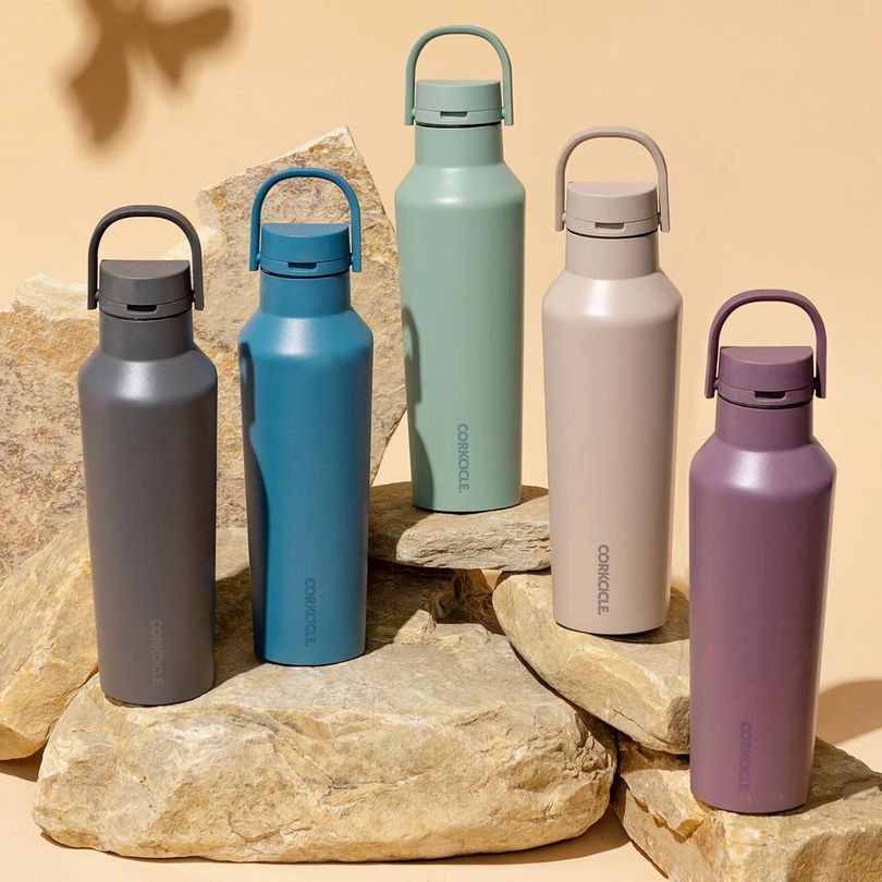 Five insulated water bottles in various colors displayed on stones.