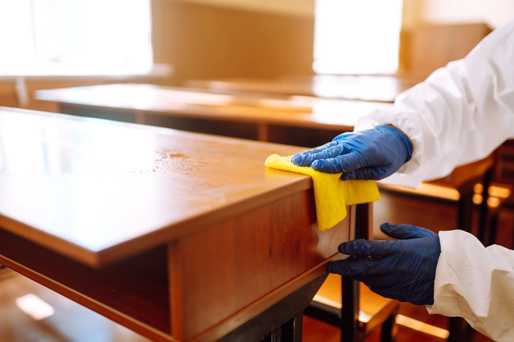 A person is cleaning a desk in a classroom with a cloth.
