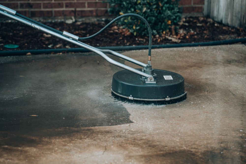 A person is cleaning a concrete driveway with a machine.