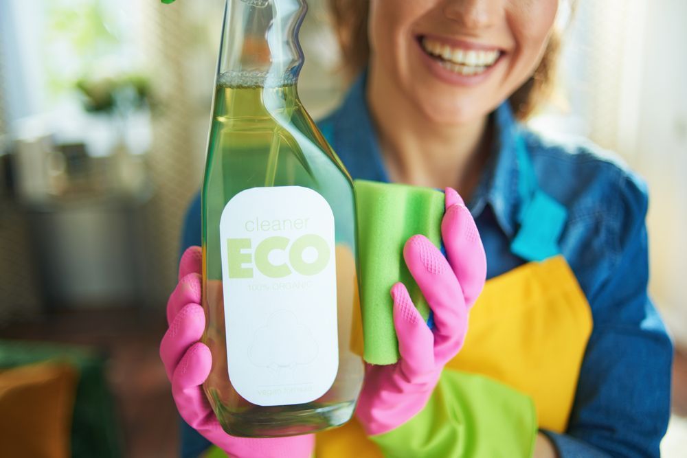 A woman in pink gloves is holding a spray bottle and a cloth.