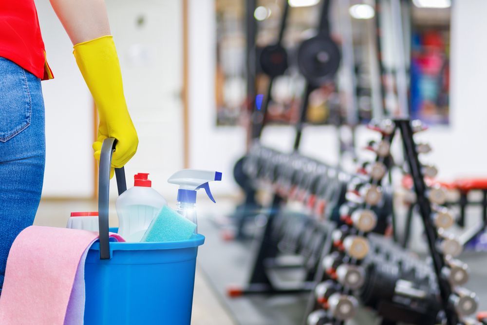 A woman is cleaning a gym with a bucket of cleaning supplies.