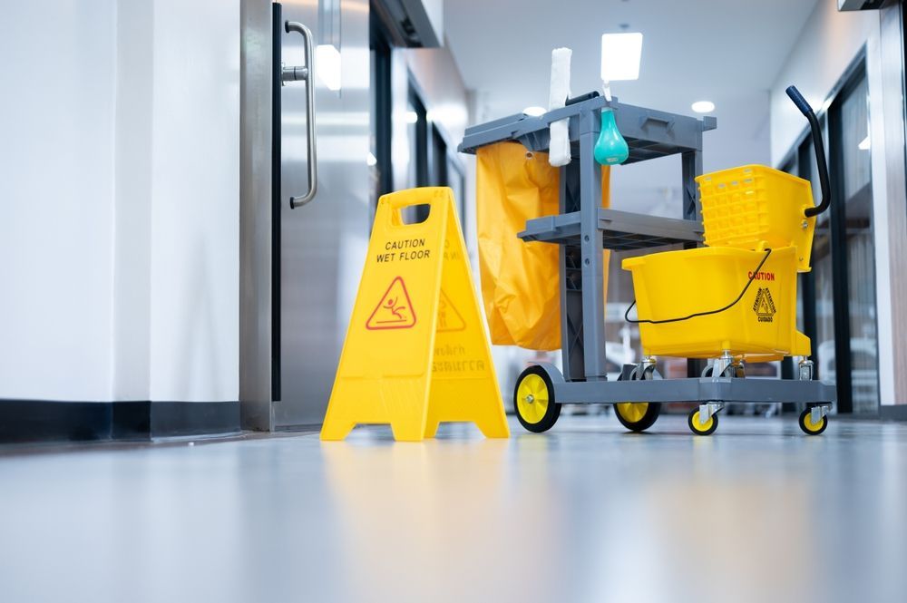 A yellow caution sign is sitting next to a cleaning cart in a hallway.