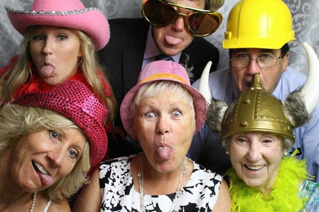Group of people in photo booth sticking out their tongues, wearing silly hats and glasses.