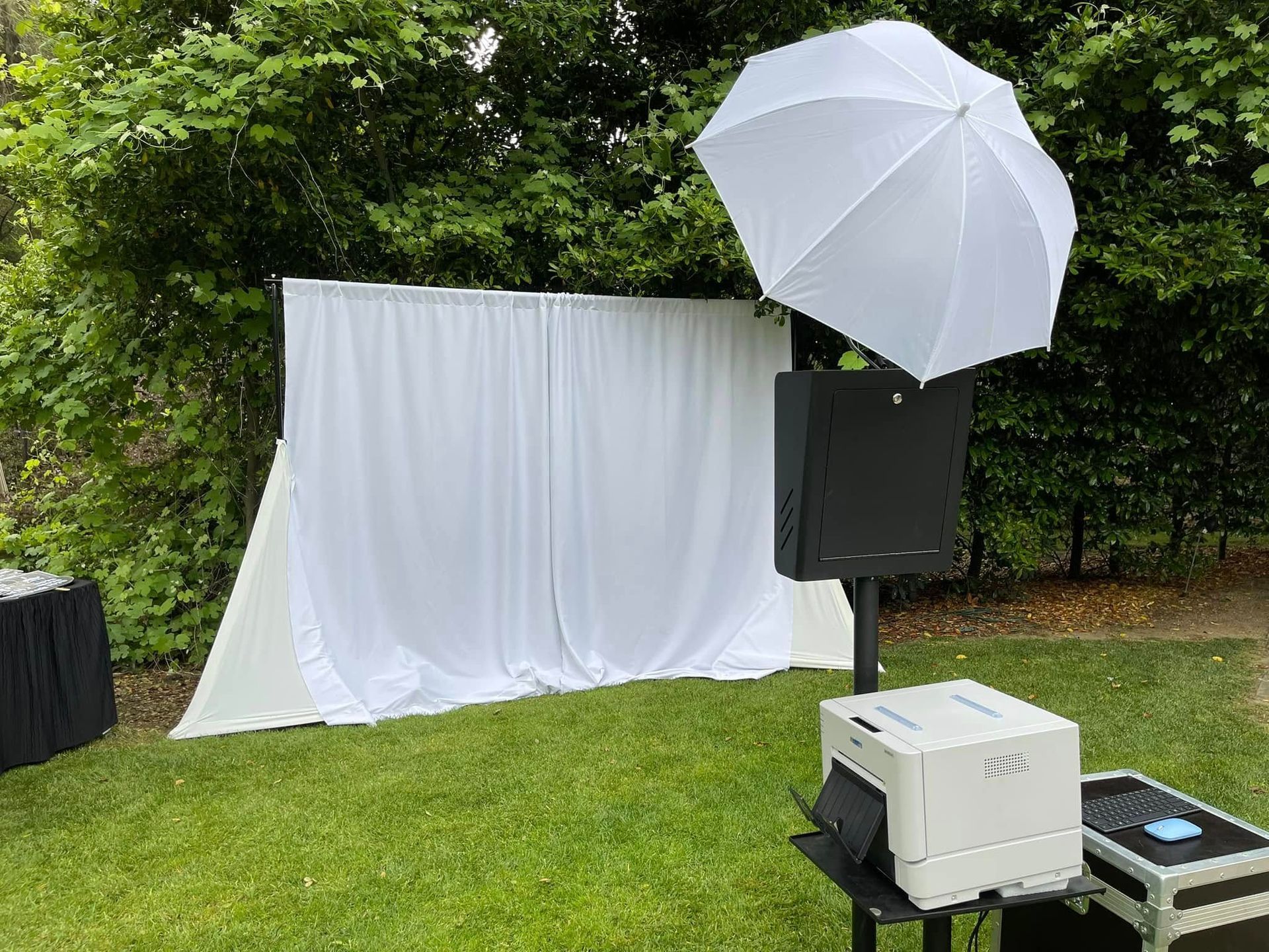 Group poses at a photo booth with props, under a canopy. A camera is visible.