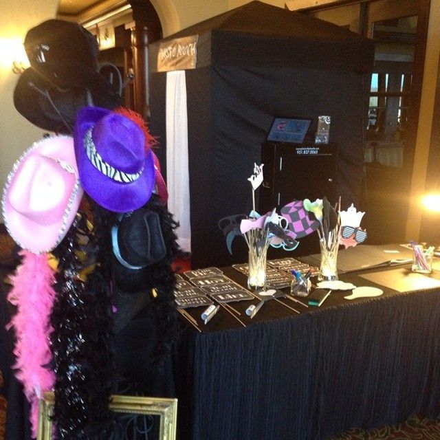 Photo booth setup with props: hats, boa, masks, and a black curtain backdrop. Table with props displayed.