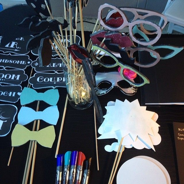 Photo booth props on a black surface: bow ties, speech bubbles, glasses, mustaches, and signs with wooden sticks.