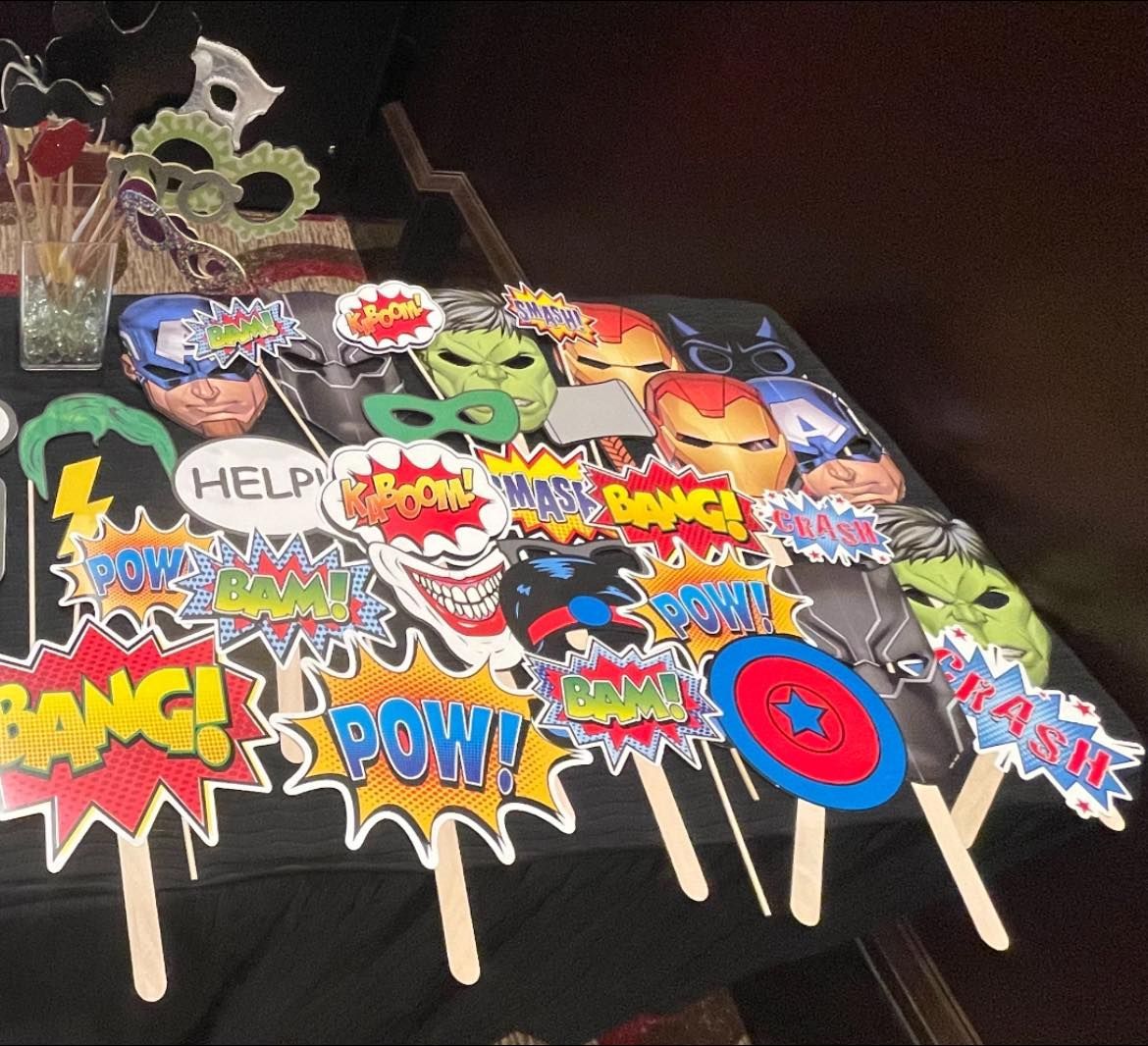 Superhero photo booth props on a black table: masks, speech bubbles with 