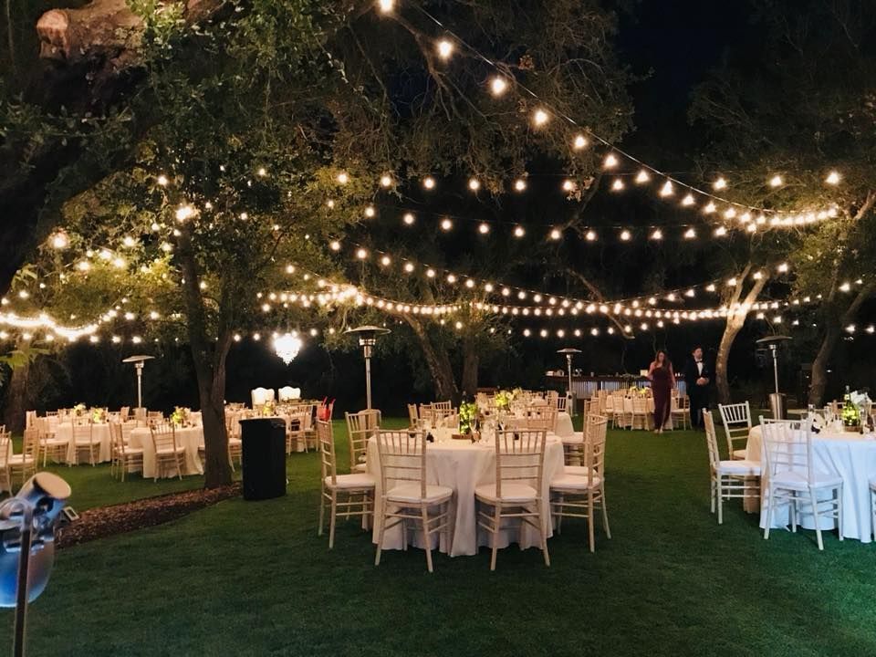 Outdoor evening wedding reception with string lights, tables, and guests.