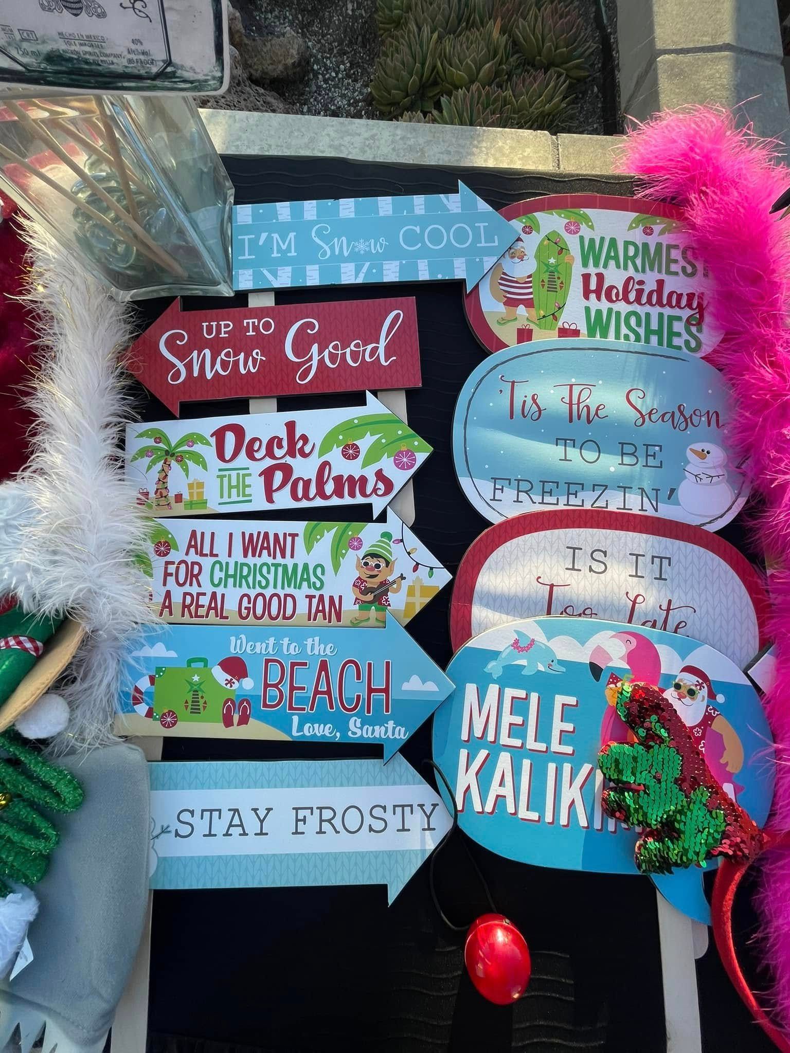 Holiday-themed directional signs on a dark background. Signs have festive sayings and tropical graphics.