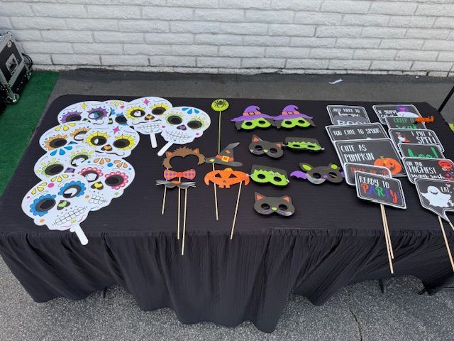 Halloween photo booth props on a black table: skull masks, witch hats, signs, and other festive items.
