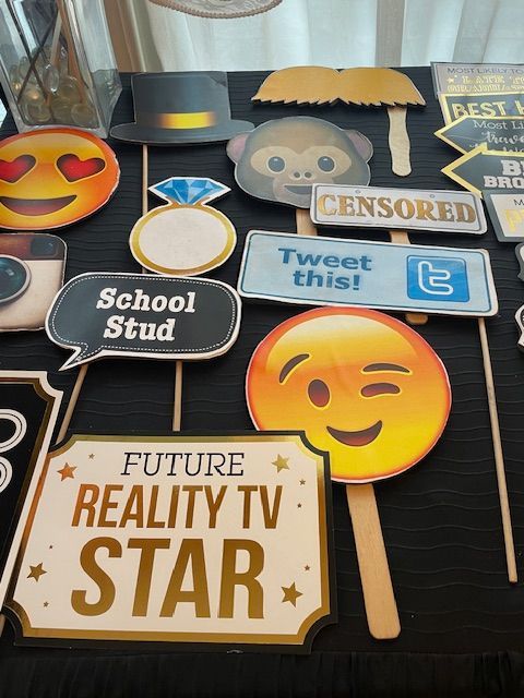 Photo booth props on a table. Includes emojis, signs with text like 
