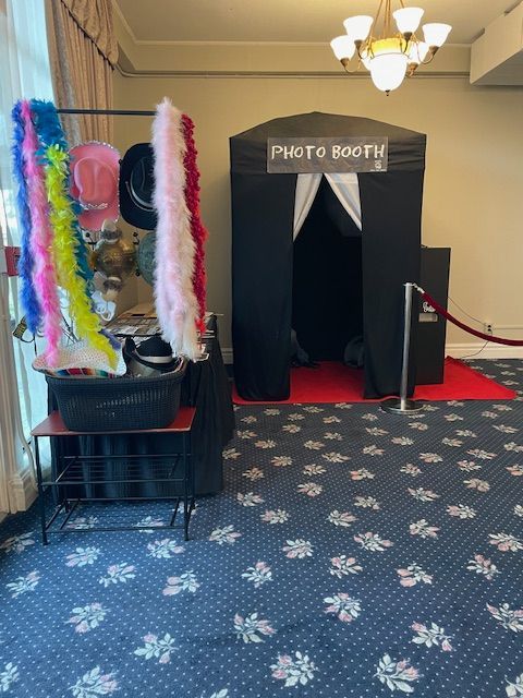 Group poses for a photo near a photo booth, with props, against a green leafy backdrop.
